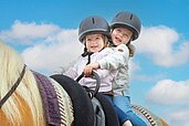 Zwei Kinder sitzen auf einem Pferd und lächeln in die Kamera im Familienhotel Familien Resort Petschnighof in Kärnten.