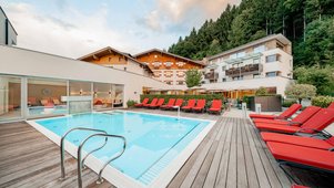 Moderner Außenpool mit roten Liegen, Holzterrasse und Blick auf die Hotelgebäude des Familienhotels Amiamo.