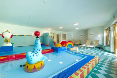 Der Kinderpool im Familienhotel Ramsi in Kärnten ist bunt gestaltet und mit Wasserspielen ausgestattet, bequeme Liegen bieten Platz für entspannte Pausen