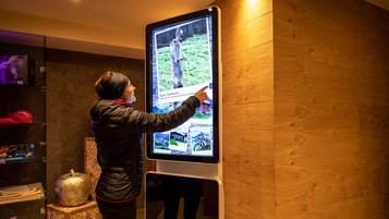 Gast bedient einen interaktiven Informationsscreen im Lobbybereich des Familienhotels Galtenberg