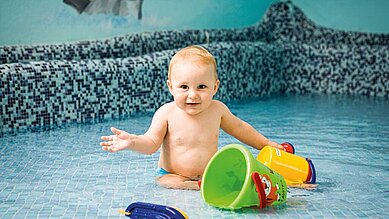 Baby sitzt mit Spielsachen im Babybecken des Familienhotels Sonnenpark.