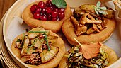 Eine Auswahl an traditionellen österreichischen Gerichten, präsentiert in einem Dampfkorb, darunter Knödel mit verschiedenen herzhaften Toppings wie Speck, Pilzen und frischen Kräutern im Hotel Habachklause.