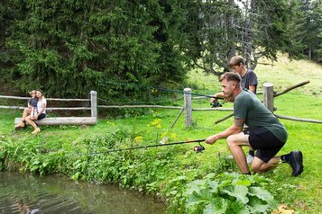 Vater und Sohn fischen am Bach im Familienurlaub im Familienhotel Hochegger