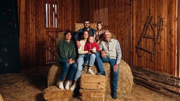 Mehrgenerationenfamilie sitzt auf Heuballen in einer rustikalen Scheune im Familienhotel Huber in Südtirol