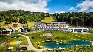 Das Familienhotel Petschnighof in Kärnten, umgeben von einem großen Outoor Hotelgelände mit Trampolin, Badeteich und vielen weiteren Spielmöglichkeiten für Kinder.