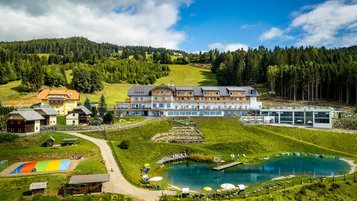 Das Familienhotel Petschnighof in Kärnten, umgeben von einem großen Outoor Hotelgelände mit Trampolin, Badeteich und vielen weiteren Spielmöglichkeiten für Kinder.
