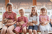 Vier Mädchen sitzen mit Hasen auf dem Schoß auf einer Fensterbank im Kleintierbereich des Familienhotels Huber in Südtirol.