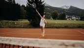 Person spielt Tennis auf dem Tennisplatz beim Hotel Sonngastein im Salzburger Land mit Bergen im Hintergrund.