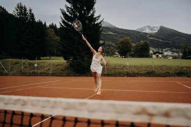 Person spielt Tennis auf dem Tennisplatz beim Hotel Sonngastein im Salzburger Land mit Bergen im Hintergrund.