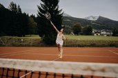 Person spielt Tennis auf dem Tennisplatz beim Hotel Sonngastein im Salzburger Land mit Bergen im Hintergrund.
