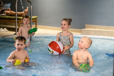 Kleinkinder plantschen und spielen im flachen Kinderbecken des Zauchenseehof, fröhlich mit Wasserpistolen und Ball beschäftigt.