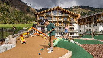Kinder spielen Minigolf auf dem Abenteuerspielplatz des Familienhotels Almfamilyhotel Scherer mit Blick auf die umliegende Berglandschaft.