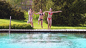 Drei Mädchen springen in den Outdoor Natur Pool des Familienhotels Landgut Furtherwirt in Tirol.