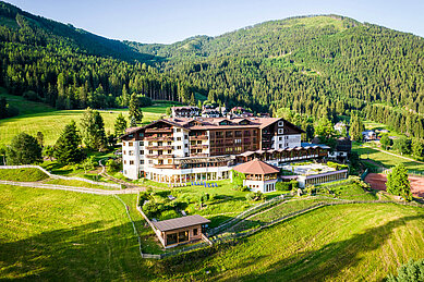 Das Familienhotel Kircheimerhof in Kärnten von außen im Sommer, umgeben von einer großen Grünfläche.