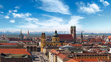 Blick auf die Stadt München von oben mit einem schönen Alpenpanorama im Hintergrund.