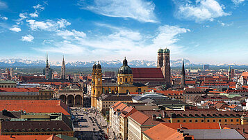 Blick auf die Stadt München von oben mit einem schönen Alpenpanorama im Hintergrund.