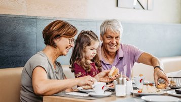 Familie mit Kind frühstückt gemeinsam im AIGO Welcome Family Restaurant am gedeckten Tisch.