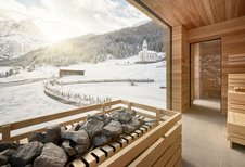Sauna mit Aufgussbereich und Blick durch das Fenster auf eine verschneite Winterlandschaft im Hotel Bella Vista in Südtirol.