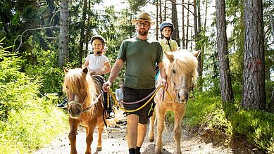 Zwei Kinder bei einem geführten Ponyausritt im Wald im Familienhotel Lärchenhof in Tirol