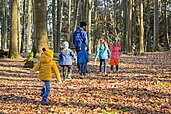 Kinder laufen zusammen mit dem Kinderbetreuer durch das Laub im Wald im Waldkinderclub des Familienhotels Landhaus zur Ohe.