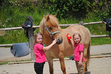 Zwei Mädchen striegeln ein Pony im Familienhotel Familien Resort Petschnighof in Kärnten.