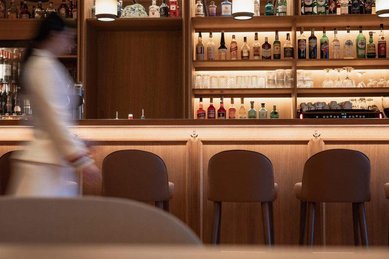 Innenansicht einer Bar mit beleuchteten Regalen und Barhockern im Familienhotel Bella Vista in Suedtirol.