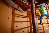 m Familienhotel der Ponyhof Steiermark klettert ein Kind im Indoor Bereich die Wand hoch.