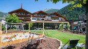 Kinder spielen auf aus dem aus Holz gebauten Outdoor-Spielplatz mit großer Röhrenrutsche im Familienhotel Huber in Südtirol.