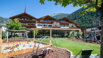 Kinder spielen auf aus dem aus Holz gebauten Outdoor-Spielplatz mit großer Röhrenrutsche im Familienhotel Huber in Südtirol.