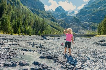 Ein Kind spielt nahe dem Familienhotel Bella Vista in Südtirol in einem Bachbett mit Blick auf die Berge.