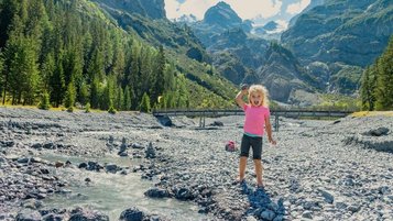 Ein Kind spielt nahe dem Familienhotel Bella Vista in Südtirol in einem Bachbett mit Blick auf die Berge.