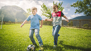 Zwei jugendliche Jungs spielen draußen auf dem Außengelände des Familienhotels Landgut Furtherwirt Fußball.