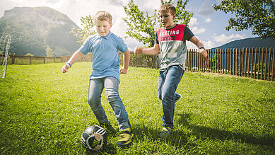Zwei jugendliche Jungs spielen draußen auf dem Außengelände des Familienhotels Landgut Furtherwirt Fußball.