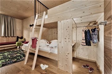 Eine Familiensuite im Familienhotel Mia Alpina in Tirol mit Hochbett, Kinderkleidung, Wohnbereich und hellen Holzelementen.