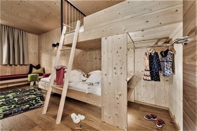 Eine Familiensuite im Familienhotel Mia Alpina in Tirol mit Hochbett, Kinderkleidung, Wohnbereich und hellen Holzelementen.