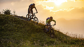 Radfahren im Salzburger Land: Pärchen mit dem Mountainbike über die Berge bei Abendsonne.