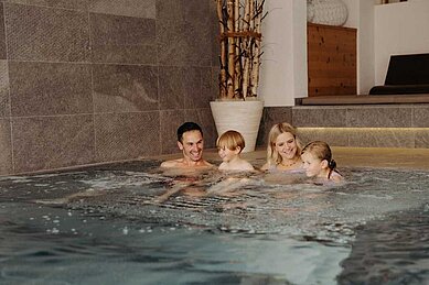 Eine glückliche Familie entspannt zusammen im Indoor-Pool des Hotels Habachklause im Salzburger Land.