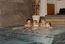 Eine glückliche Familie entspannt zusammen im Indoor-Pool des Hotels Habachklause im Salzburger Land.