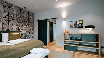 Modernes, gemütliches Zimmer im Landhaus Averbeck mit gemusterter Akzentwand, großem Bett, Schiebetüren und stilvollem Sideboard.