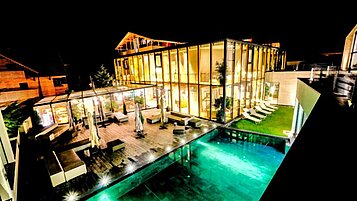 Das Familienhotel Ulrichshof im Bayerischen Wald von außen bei Nacht. Zu sehen ist ein großer beleuchteter Pool und eine großzügige Liegefläche.