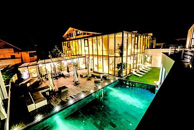 Das Familienhotel Ulrichshof im Bayerischen Wald von außen bei Nacht. Zu sehen ist ein großer beleuchteter Pool und eine großzügige Liegefläche.
