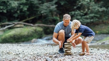 Vater und Sohn bauen einen Turm aus Steinen am Bach.