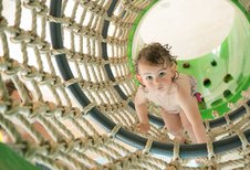 Ein neugieriges Kleinkind klettert mutig durch ein großes Seilnetz im Wasserspielbereich des Landguts Furtherwirt