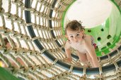  Ein neugieriges Kleinkind klettert mutig durch ein großes Seilnetz im Wasserspielbereich des Landguts Furtherwirt