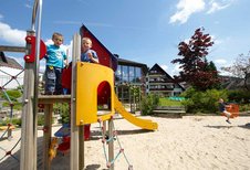 Zwei Jungs stehen auf dem Spielturm mit gelber Rutsche auf dem Außenspielplatzes des Familienhotels Sonnenpark.