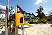 Zwei Jungs stehen auf dem Spielturm mit gelber Rutsche auf dem Außenspielplatzes des Familienhotels Sonnenpark.