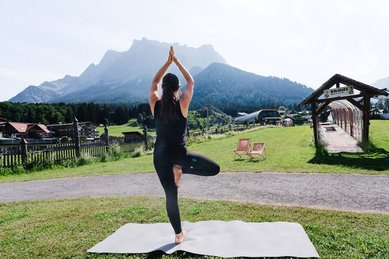 Eine Frau macht Yoga auf einer Matte vor der beeindruckenden Bergkulisse der Tiroler Zugspitzarena nahe dem Familienhotel Tirolerhof.