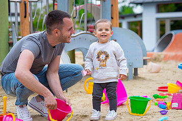 Papa spielt mit seinem Sohn im Sandkasten auf dem Außengelände des Familienhotels Kolping Hotel Spa & Family Resort in Ungarn.