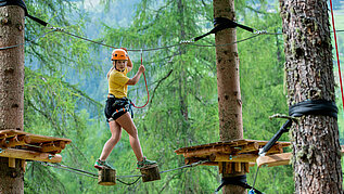 Mädchen klettert im Hochseilgarten in Tirol.