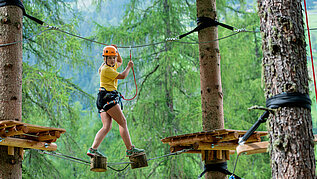 Mädchen klettert im Hochseilgarten in Tirol.